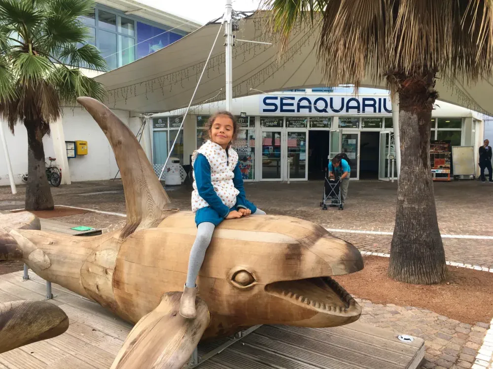 Fotografía de diegoenfrance.com: niña sonriendo sobre una escultura de delfín frente al Seaquarium de Grau-du-Roi.