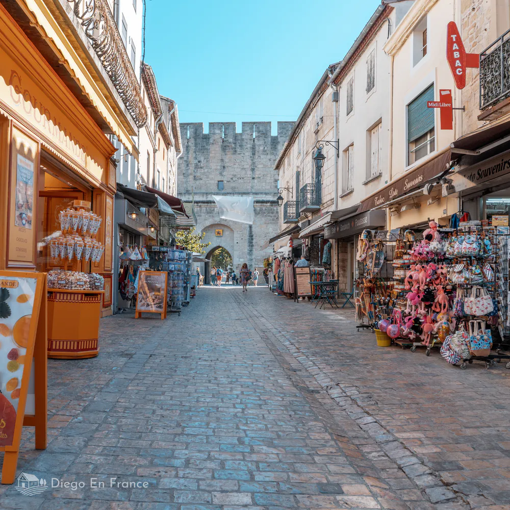 Calles empedradas y tiendas típicas que ver en Aigues-Mortes, con la histórica muralla al fondo. Fotografía de diegoenfrance.com
