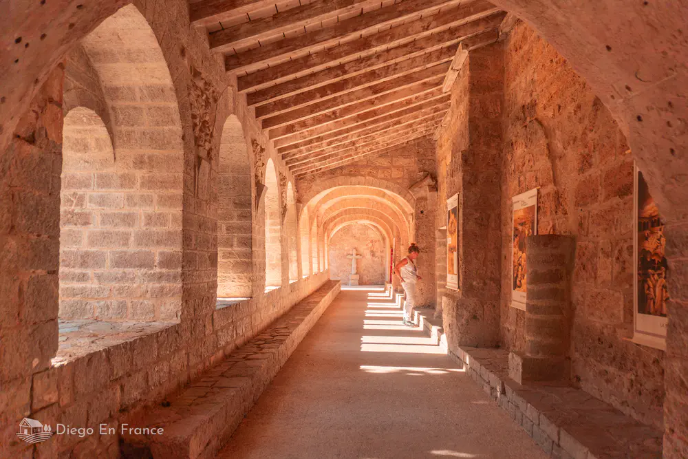 Galería cubierta de piedra con arcos y paneles expositivos en el monasterio