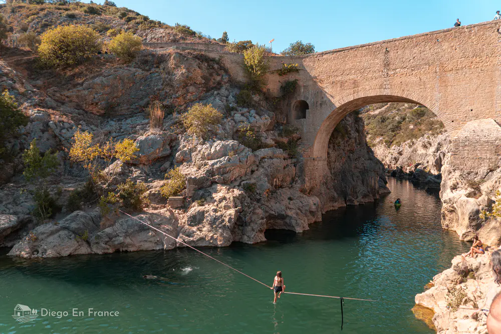Puente de piedra sobre río con personas cruzando cuerda suspendida