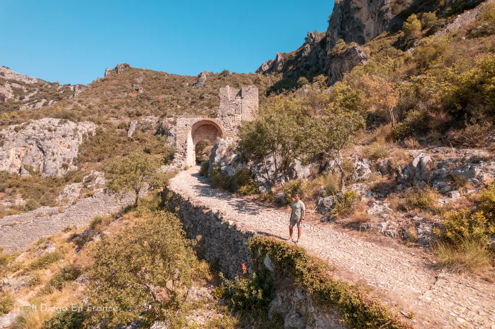 Sendero empedrado con arco medieval entre colinas rocosas cerca del pueblo