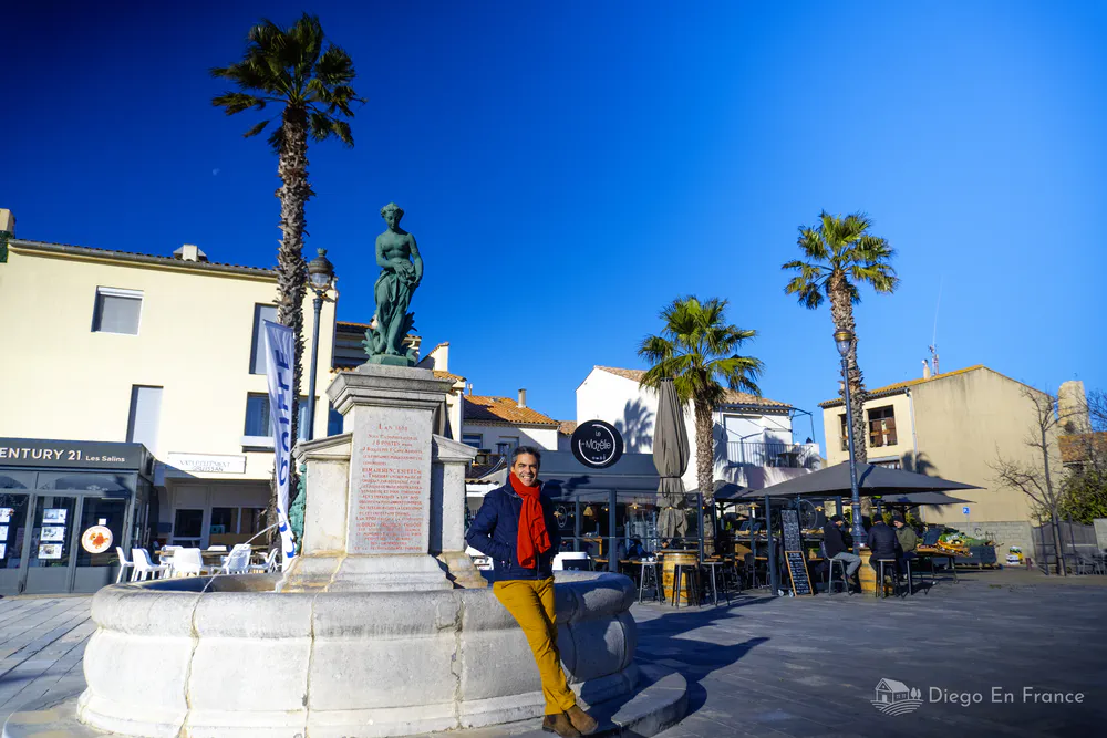 Fotografía de diegoenfrance.com de la plaza principal de Gruissan con fuente, palmeras y cafés al aire libre.