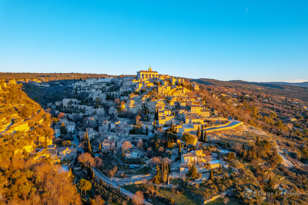 Aerial view of Gordes, one of the most beautiful villages in France, illuminated by the golden light of the sunset over the Luberon hills.