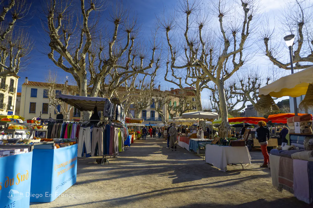 Open air market in Collioure with tourists strolling among the stalls.