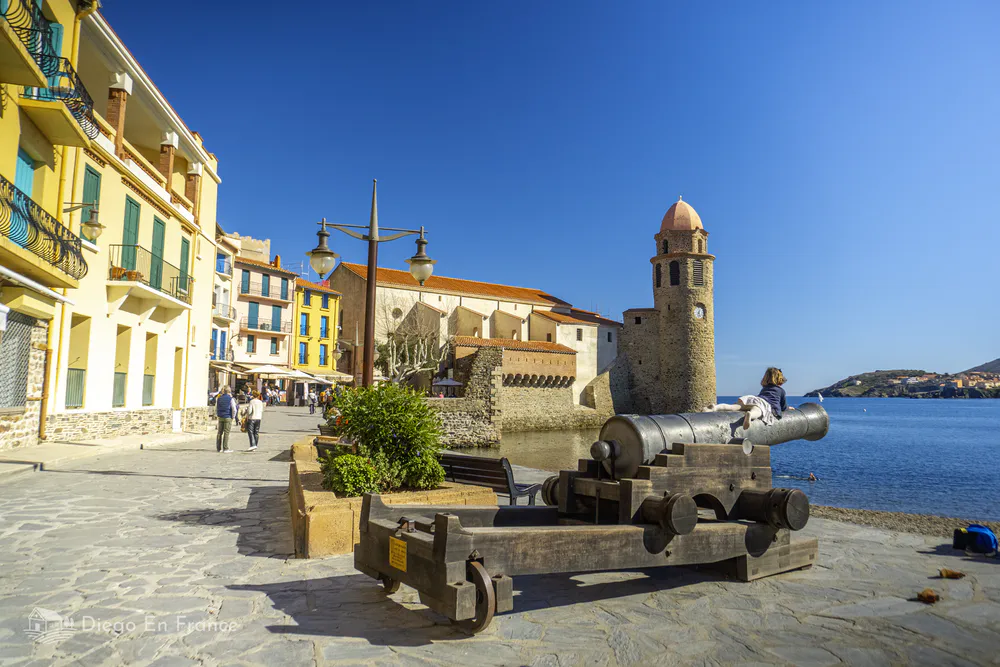 Tourists strolling along Collioure's promenade by its calm waters.