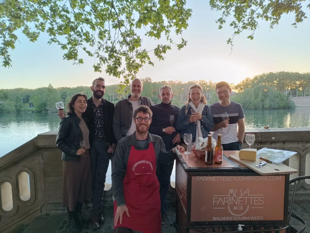 People participating in a gastronomic tour in Toulouse, tasting authentic flavors such as cured meats, cheeses and regional wines by the river.