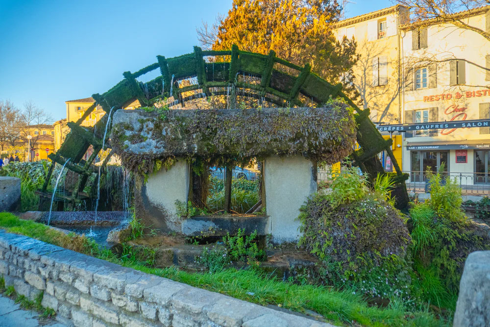 Molino de agua tradicional en funcionamiento rodeado de vegetación y arquitectura rural. Fotografía de diegoenfrance.com