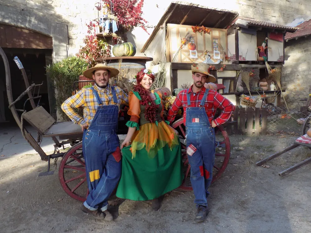 Personas disfrazadas con trajes campesinos posando junto a una carreta antigua en Le Vieux Mas.