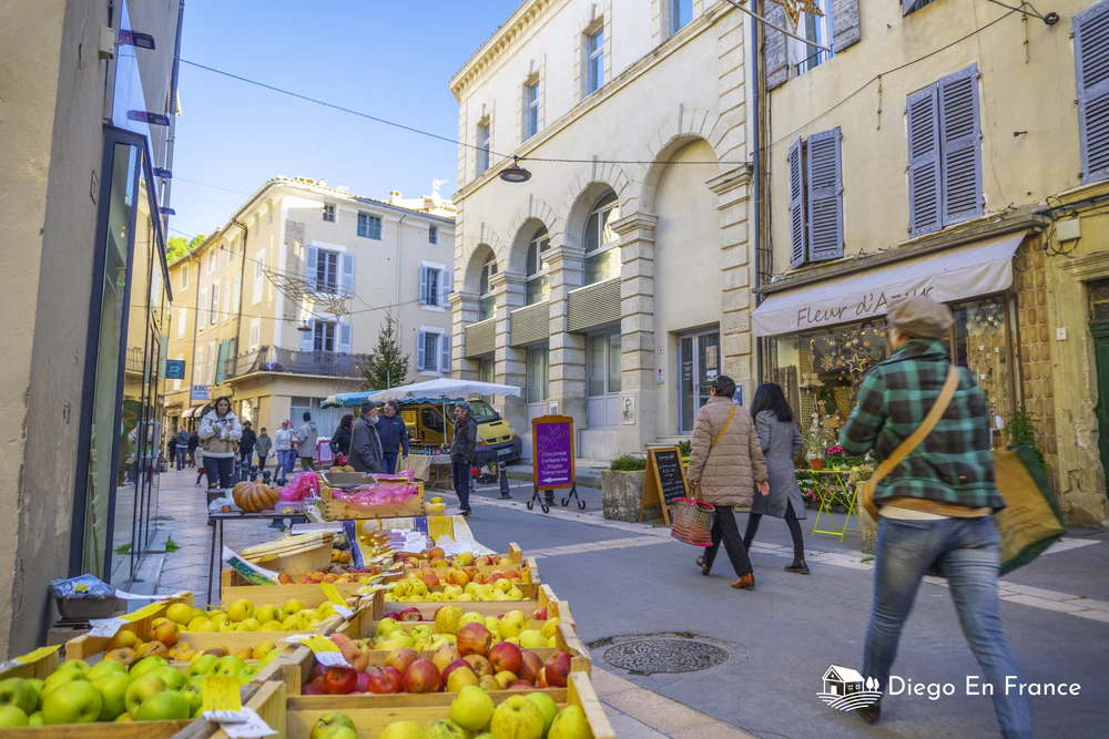 Calles animadas con puestos de frutas y productos locales en un mercado de pueblo. Fotografía de diegoenfrance.com