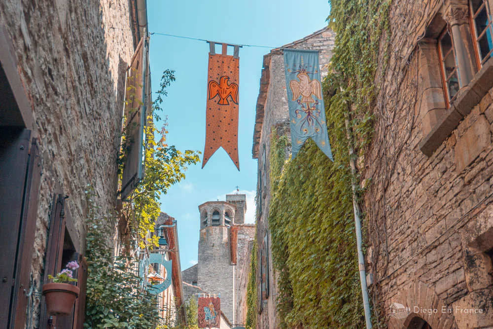 Calle estrecha con banderas medievales y torre al fondo