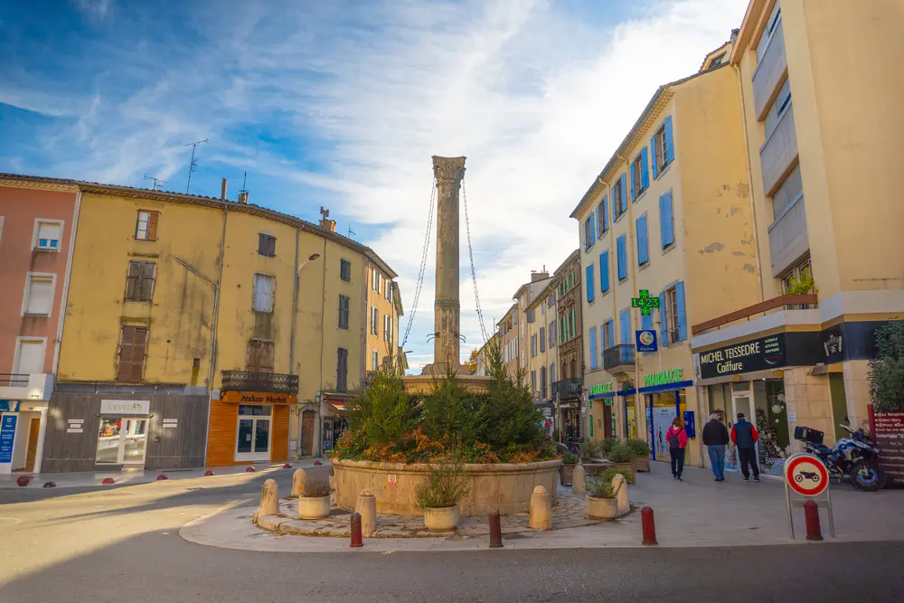 Urban square with central tower, yellow buildings, and people walking in a town in southern France