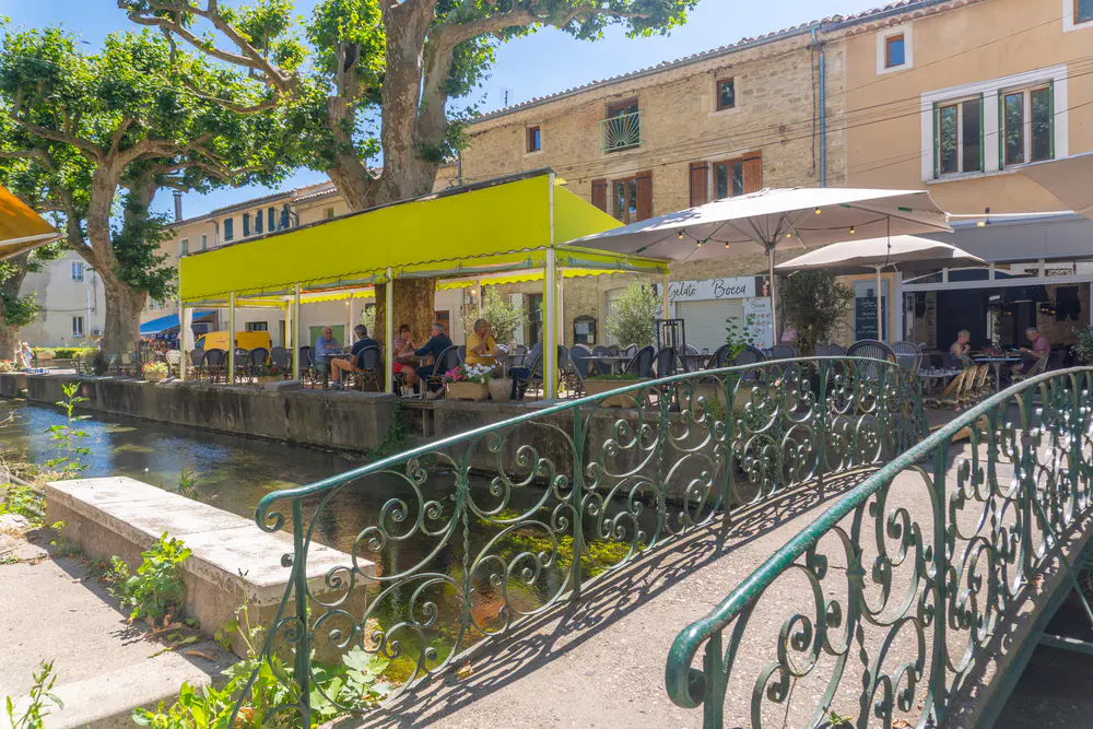 Canal with clear water, café terraces, and a small bridge in a village in southern France