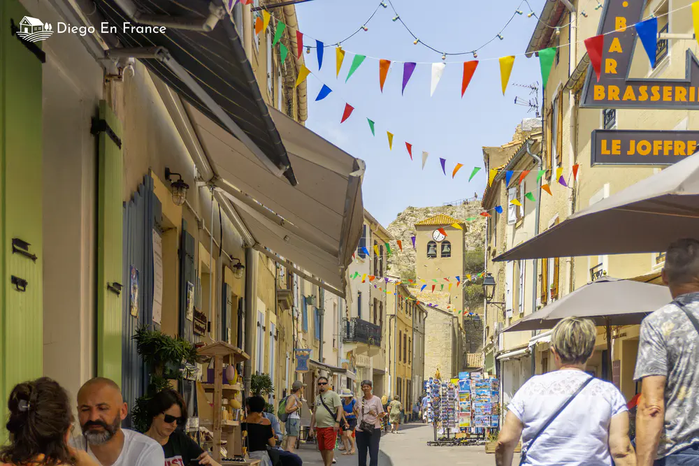 Pedestrian street with colorful flags, terraces, and people strolling among old buildings.
