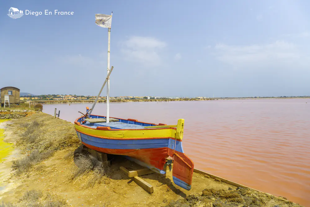 Wooden boat next to a pink water lagoon in an open natural setting.