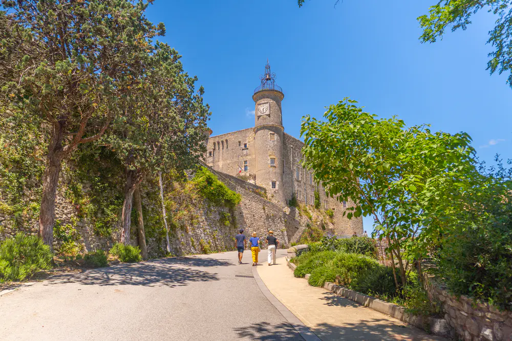 Access road with a stone wall, tower, and surrounding greenery in a village in southern France