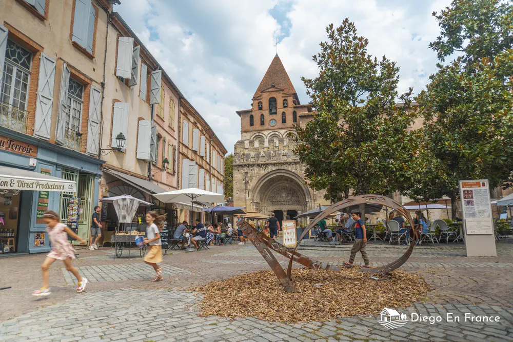 Square with modern sculpture, terraces, and Romanesque church façade
