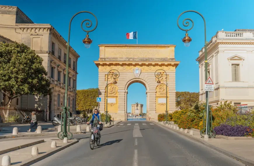 Foto de una mujer en bicicleta con el arco del trinfo en Montpellier de fondo
