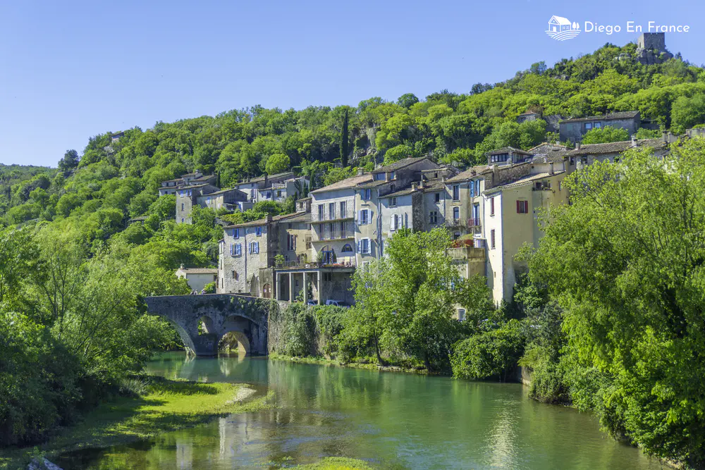 Houses lined up along a green river with a stone bridge in the south of France