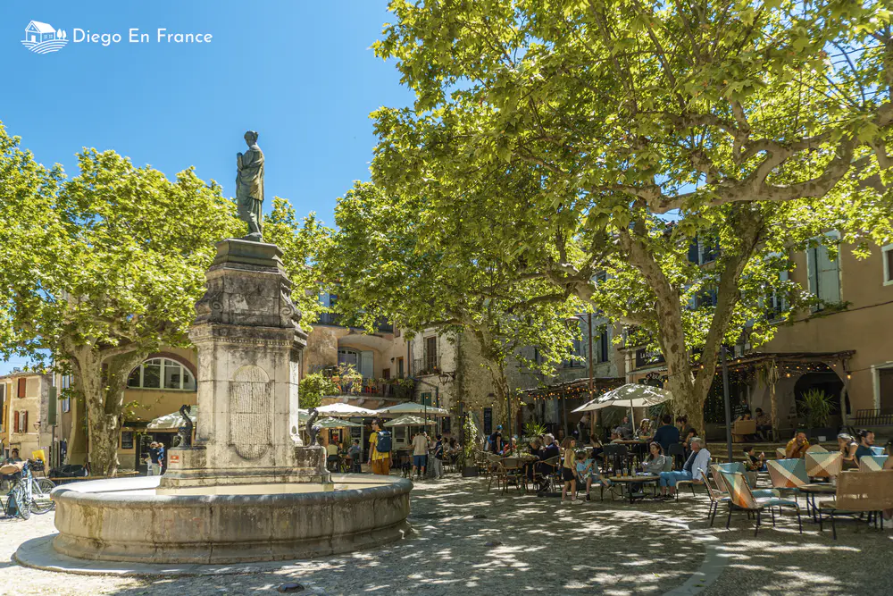 Shaded square with fountain, outdoor tables, and old buildings in the south of France
