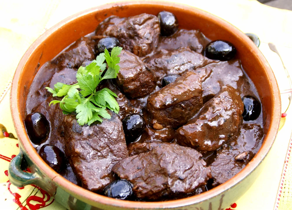 Plat de gardianne de taureau typique de Nîmes, préparé avec de la viande de taureau, des olives et une sauce au vin rouge.