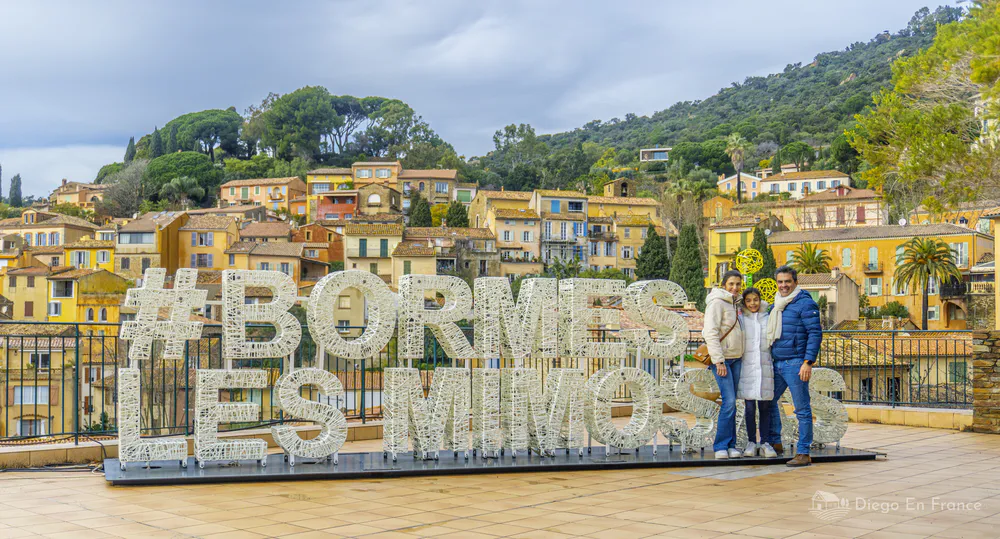 Family posing next to the Bormes-les-Mimosas sign with the colorful village in the background.