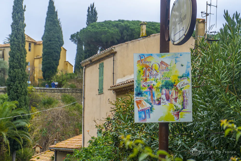 Cartel ilustrado del barrio colocado junto a casas provenzales y cipreses
