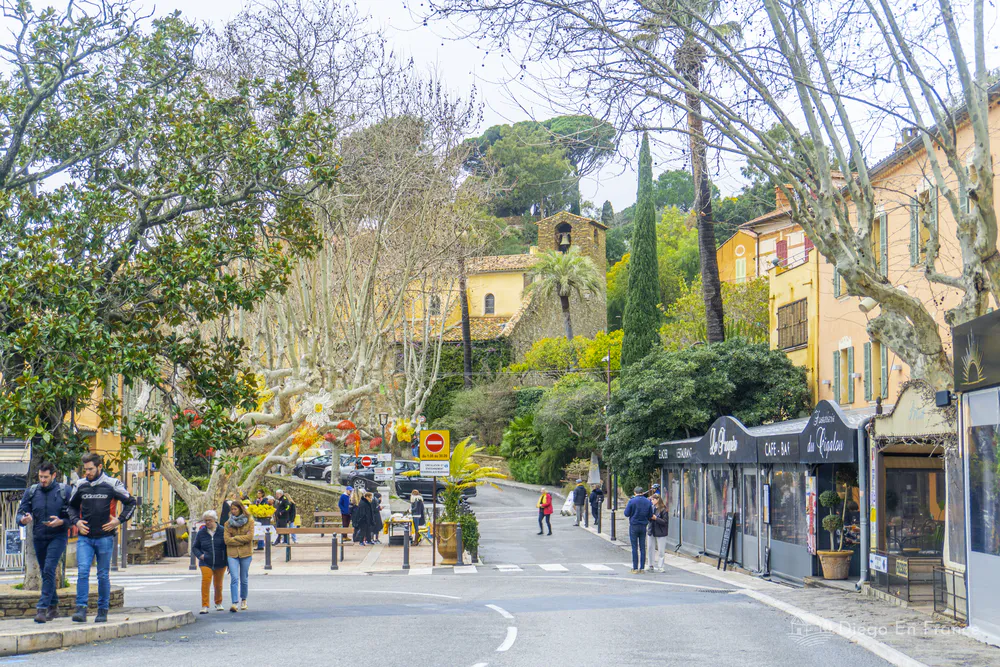 Calle arbolada con personas caminando, comercios abiertos y casas coloridas en el centro del pueblo