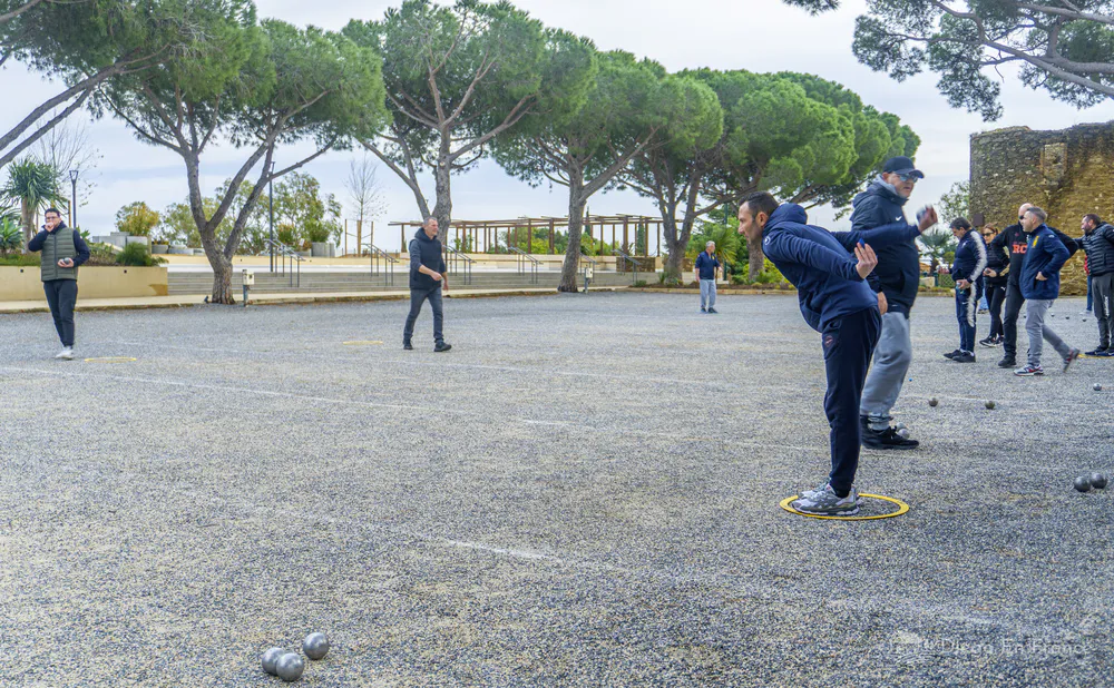 Grupo de personas jugando a la petanca en una plaza arbolada del pueblo