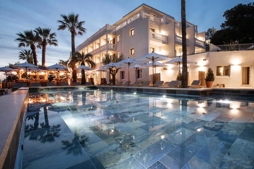 Hotel blanco iluminado al anochecer con piscina y palmeras alrededor