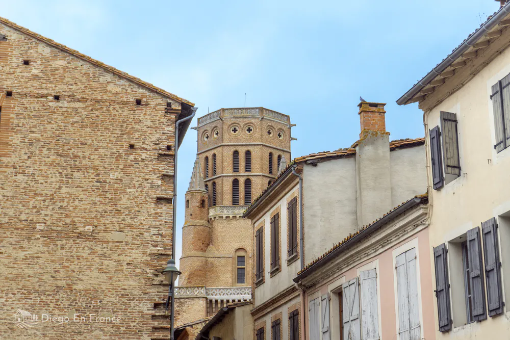 A pink brick bell tower looming between old buildings in the historic center of Lavaur.
