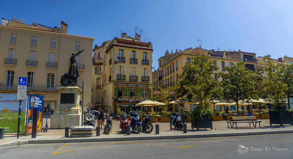 Fotografía de diegoenfrance.com mostrando una plaza céntrica con terrazas, estatua y ambiente típico del turismo en Perpiñán