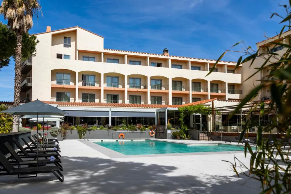 Piscina del hotel Holiday Inn Perpignan, con tumbonas, palmeras y edificio de fondo bajo cielo azul claro.