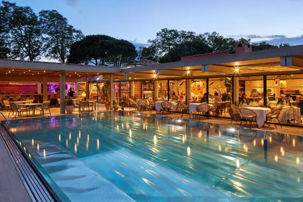 Piscina iluminada al atardecer en Villa Duflot Hôtel & Spa Perpignan, rodeada de mesas y ambiente elegante.